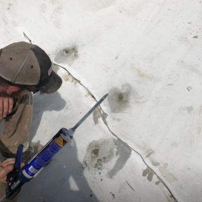 Technician applying caulk into a concrete surface crack as part of sinking porch repair in Charles Town, WV.