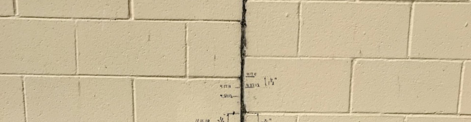 Concrete block basement wall with vertical crack and measurement markings showing signs of cracked basement wall problem in Northern Virginia.