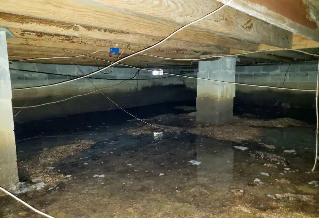 Crawl space with standing water on dirt floor and moisture stain on concrete walls causing bad crawl space odor in Alexandria, VA.
