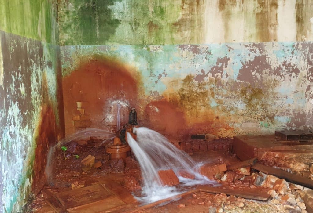 Burst pipe spraying water against a rust-stained wall, a plumbing failure as a cause of bad crawl space odor in White Post, VA.