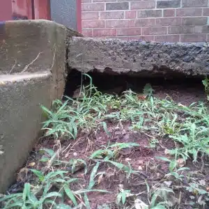Concrete porch slab separated from brick wall with visible gap and soil settlement causing sinking porch in Front Royal, VA.