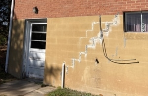 Stair step cracks zigzagging along mortar joints of exterior concrete wall, sign of cracks in basement wall problem in Ashburn, VA.