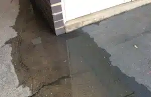 Water pooling against foundation wall on concrete surface showing drainage failure and sinking porch sign in Southbridge, VA.