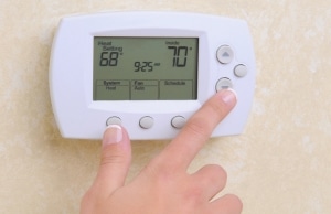 A hand adjusting a thermostat stuck degrees despite a 70 degree setting, a sign of cold floors above crawl space in Clear Brook, VA