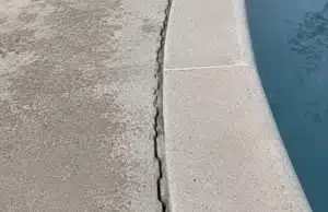 Crack forming along the edge of a concrete pool deck separating from the pool wall, sign of sinking pool deck problem in Ashburn, VA.