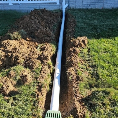 Buried downspout extension pipe installed in residential yard trench to redirect water away to fix uneven sidewalk in Berkeley, WV.