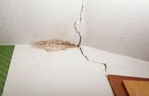 Diagonal drywall crack with water staining near a ceiling corner, a sign of foundation settlement problem in Berkeley, WV.