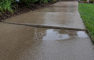 Water pooling in low depression concrete walkway after rain, a sign of uneven sidewalk in Harpers Ferry, WV.
