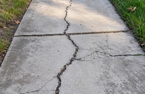 Wide cracks running across concrete sidewalk slab from soil movement beneath , a sign of uneven sidewalk in Brambleton, VA.