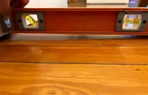 Level tool showing a sloped wood floor inside a, a sign of uneven foundation settlement in Martinsburg, WV.