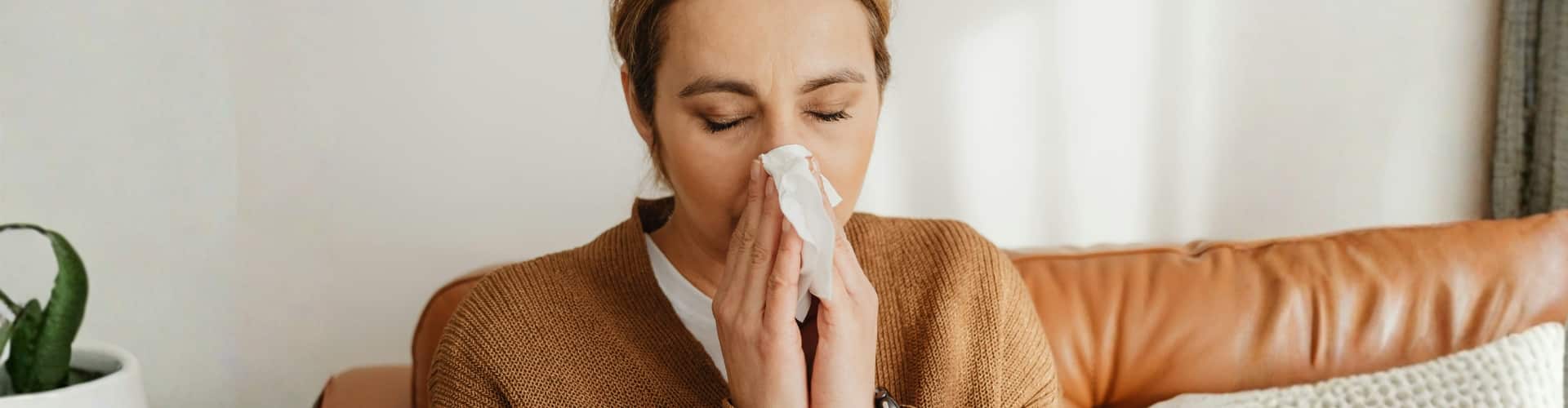 Woman sneezing into tissue showing indoor asthma and allergy symptoms from crawl space air quality problems in Northern Virginia.