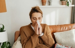 A homeowner sneezing with a tissue while sitting in living room experiencing sign of asthma or allergy symptoms in Flint Hill, VA