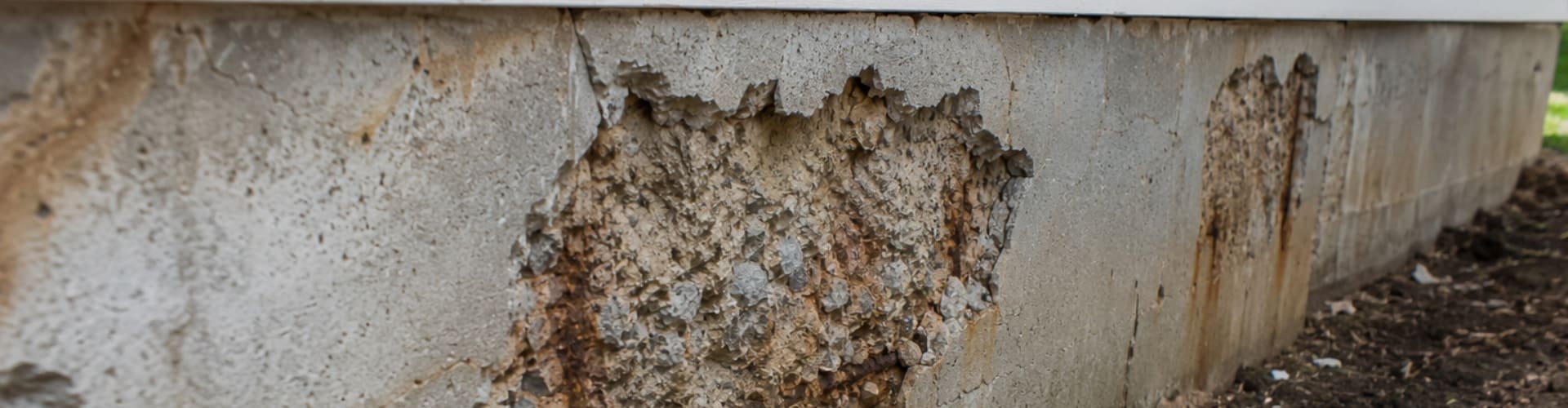 Chipping and spalling concrete on a home foundation wall with rust staining, a sign of foundation problems in Northern Virginia.