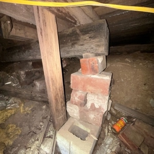 Wooden post resting on stacked old bricks in crawl space showing improper support causing an unlevel floor in Harpers Ferry, WV.