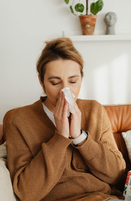 Woman sneezing on tissue experiencing asthma or allergy symptoms from poor indoor air caused by crawl space issues in Winchester, VA.