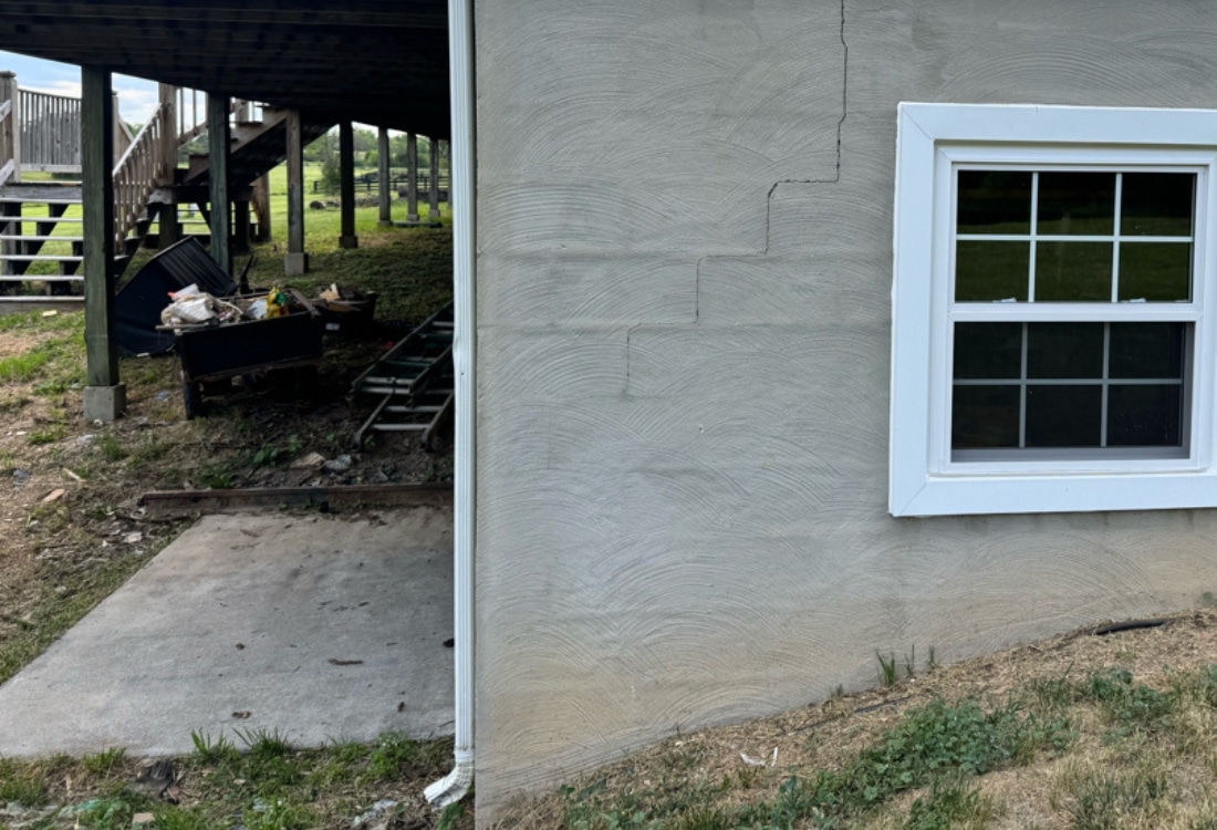 Short downspout discharging roof runoff at foundation corner contributing to soil pressure in Winchester, VA.