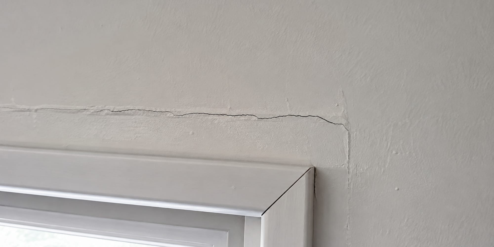 A drywall crack that keeps coming back in Northern, VA, running along the top corner of a window frame.