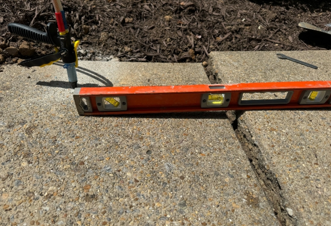 Concrete driveway lifting with a leveling bar and injection equipment correcting an uneven slab in Fairfax, VA.