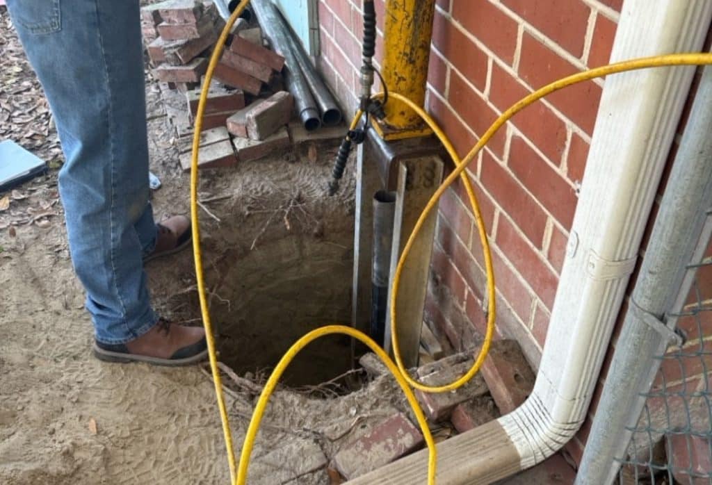 Foundation repair crew installing a push pier to stabilize cracks in brick mortar in Berryville, VA.
