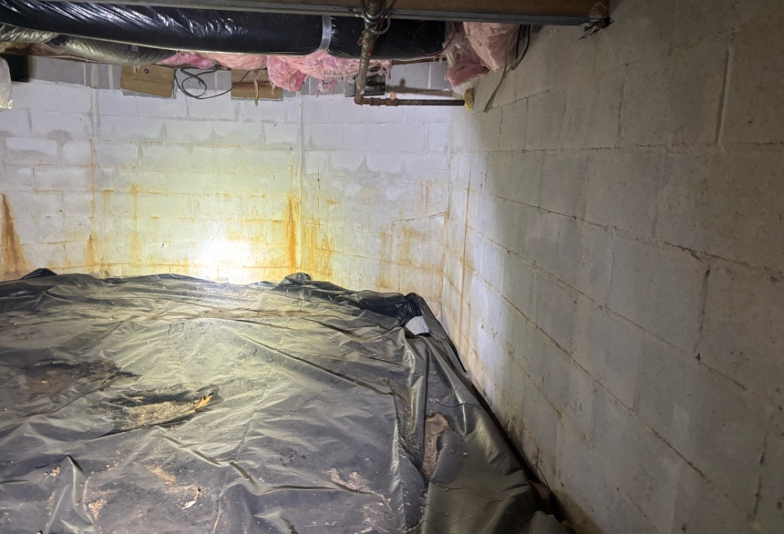 Torn black vapor barrier bunched on the floor with rust colored water stains on the crawl space block wall in Shepherdstown, WV.
