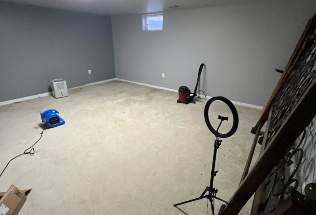 Unwaterproof finished basement in Alexandria, VA, with water damage cleanup equipment after heavy rain leak.