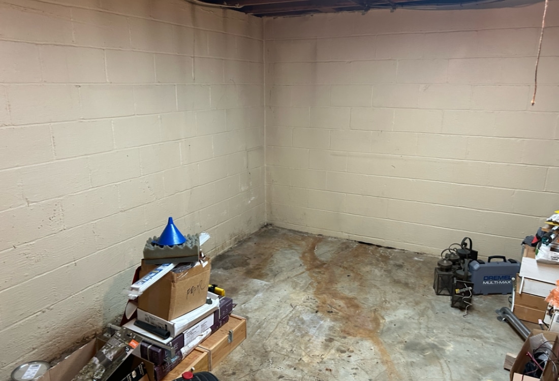 Unfinished basement with moisture stains along foundation walls and floor before renovation in Winchester, VA.