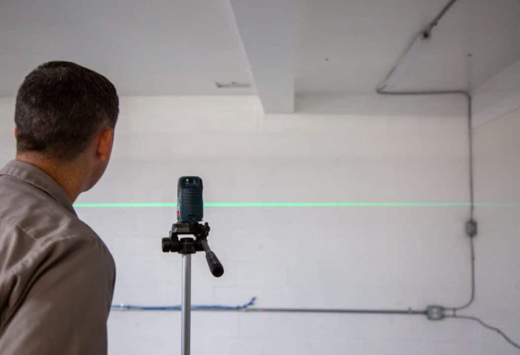 Foundation expert with a laser level during a foundation inspection of a white block wall for push pier installation in Fairfax, VA.