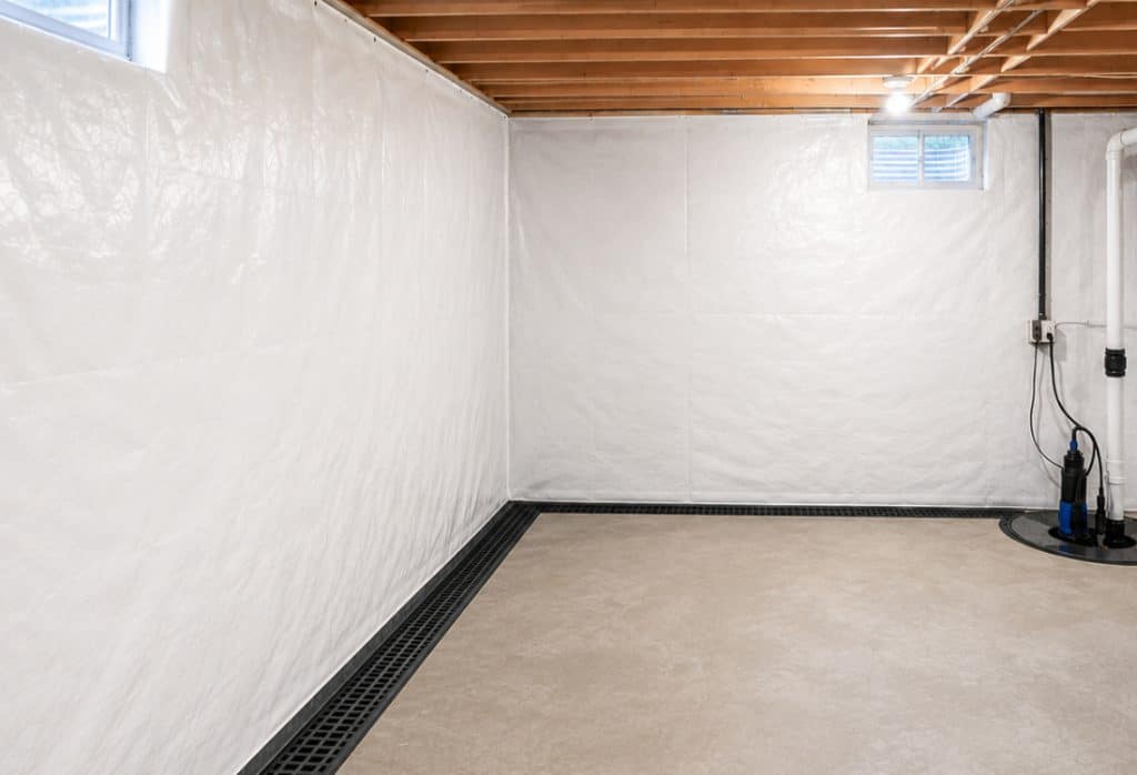 Interior basement waterproofing with white wall sheeting, a black floor-edge drain channel and a sump pump in White Post, VA