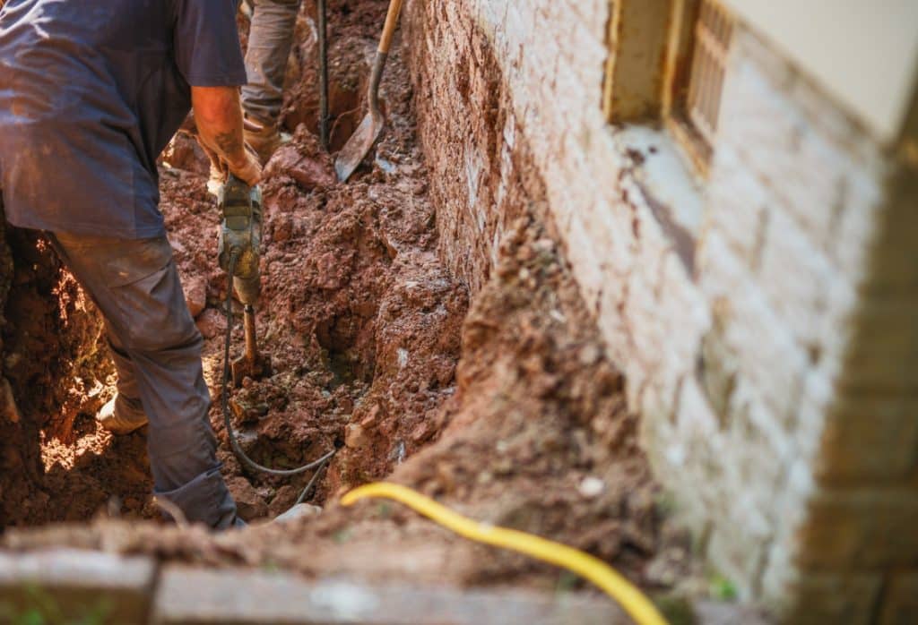 Crew working in a deep trench foundation wall in clay soil, where depth and access affect settling foundation repair cost in Reston, VA.