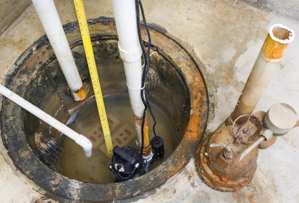 Corroded sump pump submerged in standing water inside a failing sump pit causes water in the basement in Fairfax, VA.